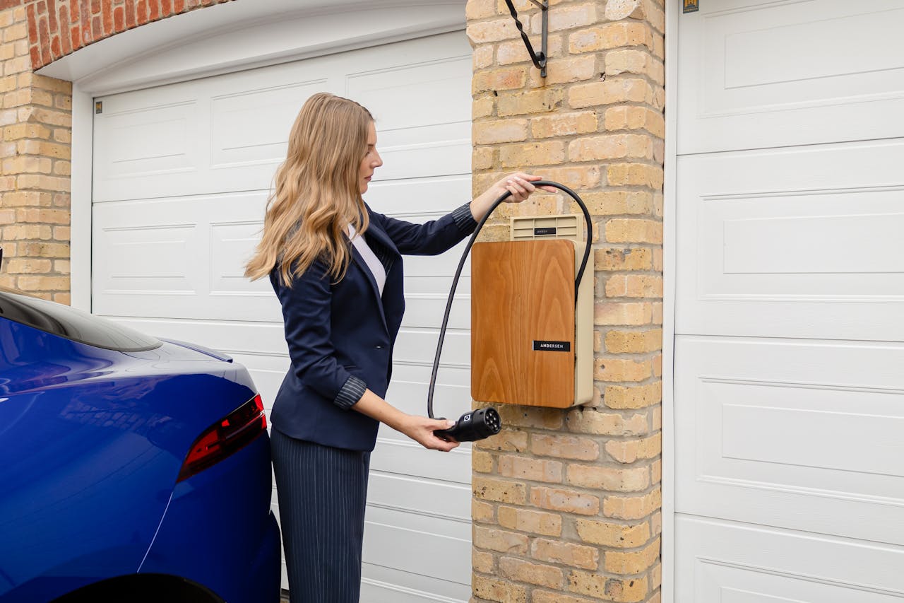A woman using a home electric vehicle charger on a brick wall in a garage.